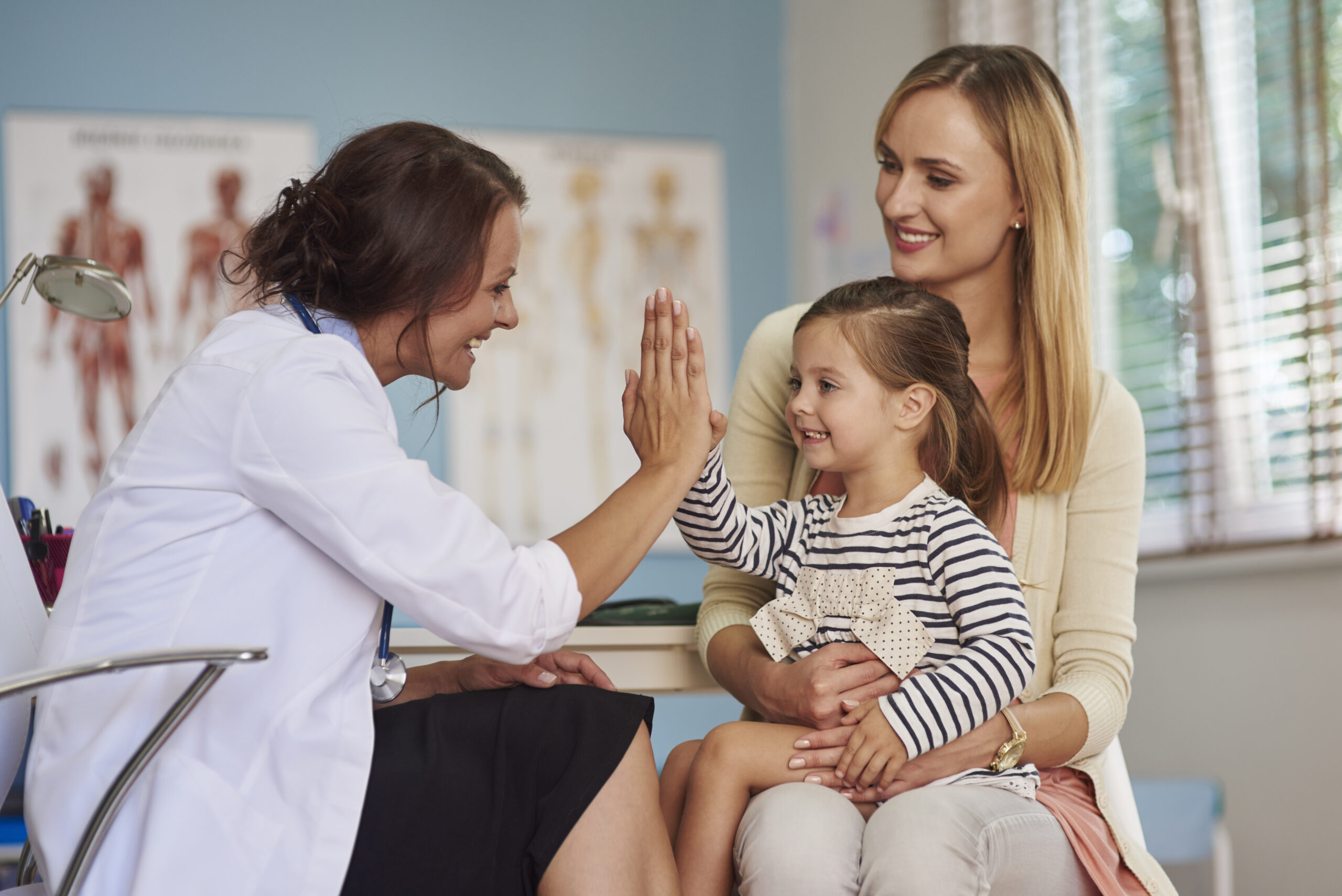 doctor giving high five smiling girl sitting her mother 039 s lap medical appointment scaled